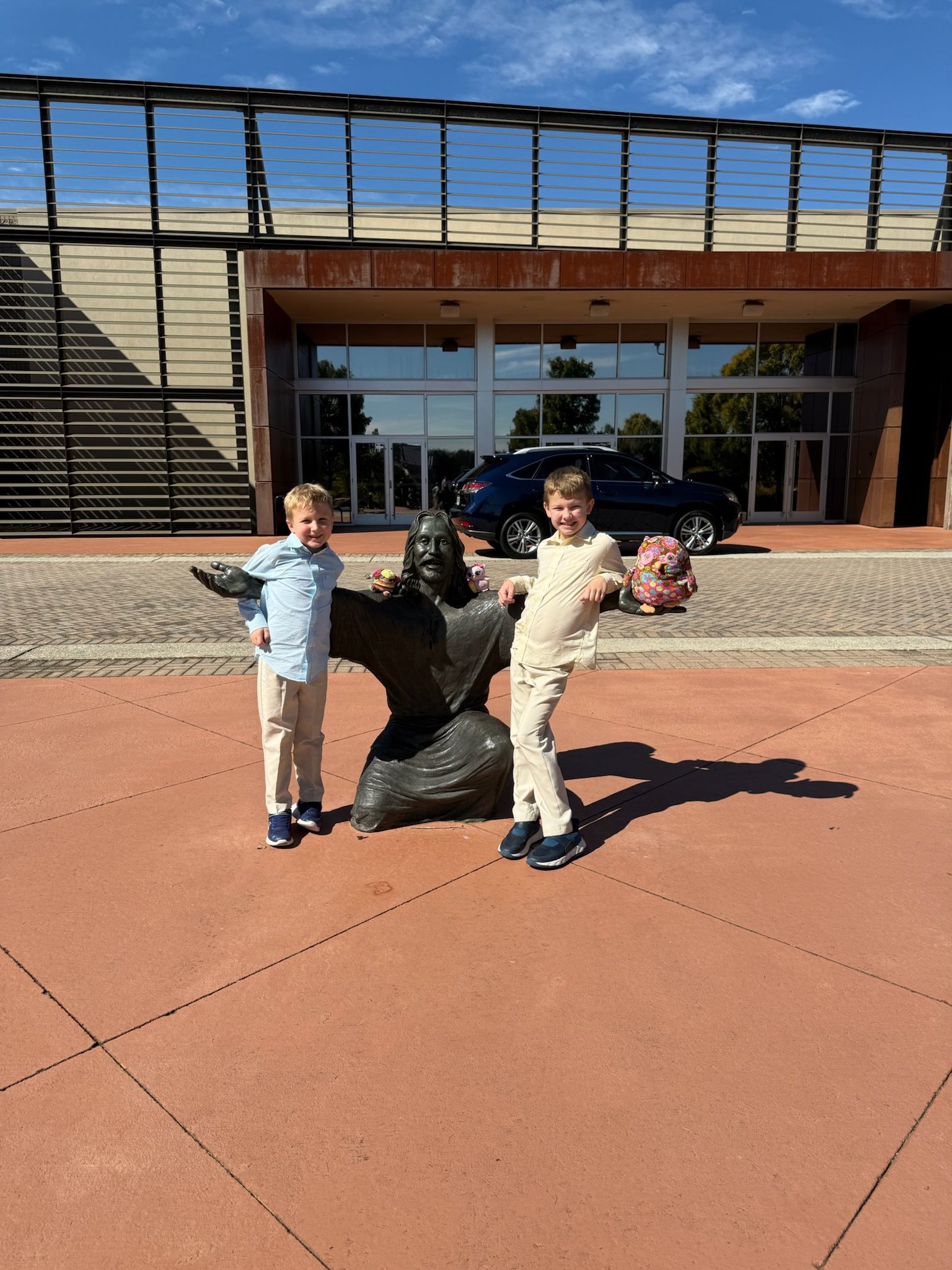 Two children pose with a bronze statue, building in background, sunny day.