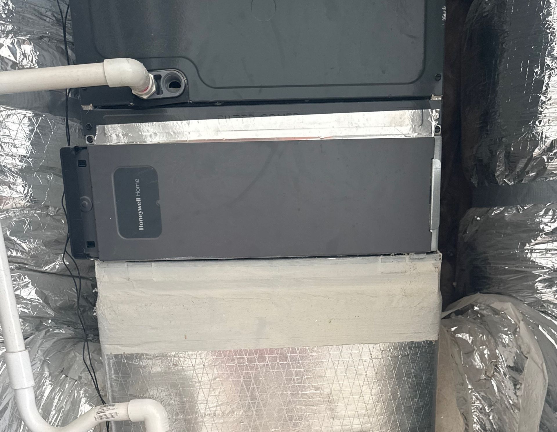 HVAC unit with a rectangular filter box, white PVC pipe, and silver insulation.