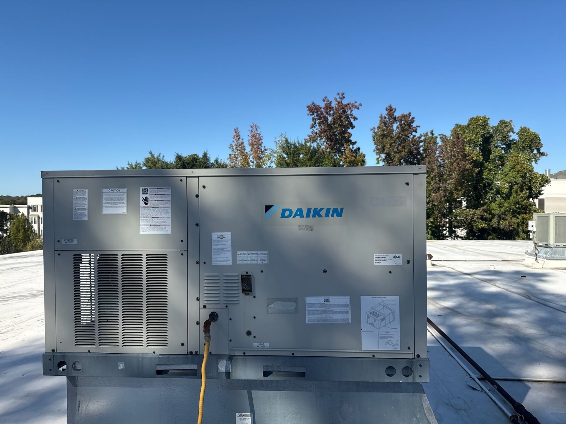 Daikin HVAC unit on rooftop with trees and a clear blue sky in background.