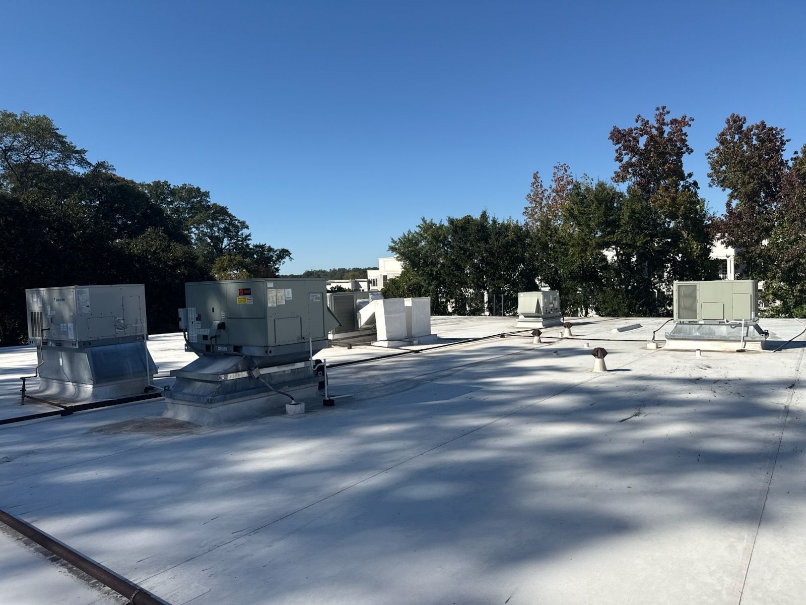 White roof with multiple HVAC units, clear sky, trees in the background.