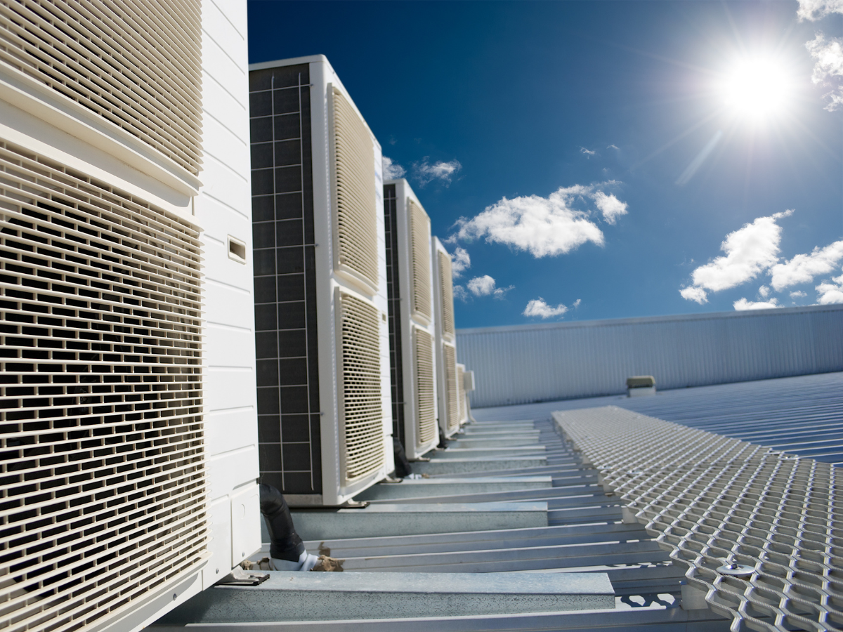 Air conditioning units on a rooftop against a blue sky with the sun.