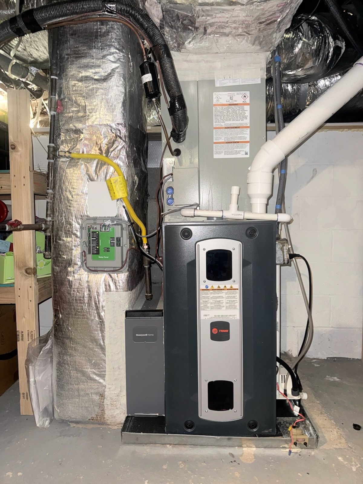 HVAC system in a basement. Silver ductwork, gray furnace and water heater. Electrical components, pipes, and gray floor.