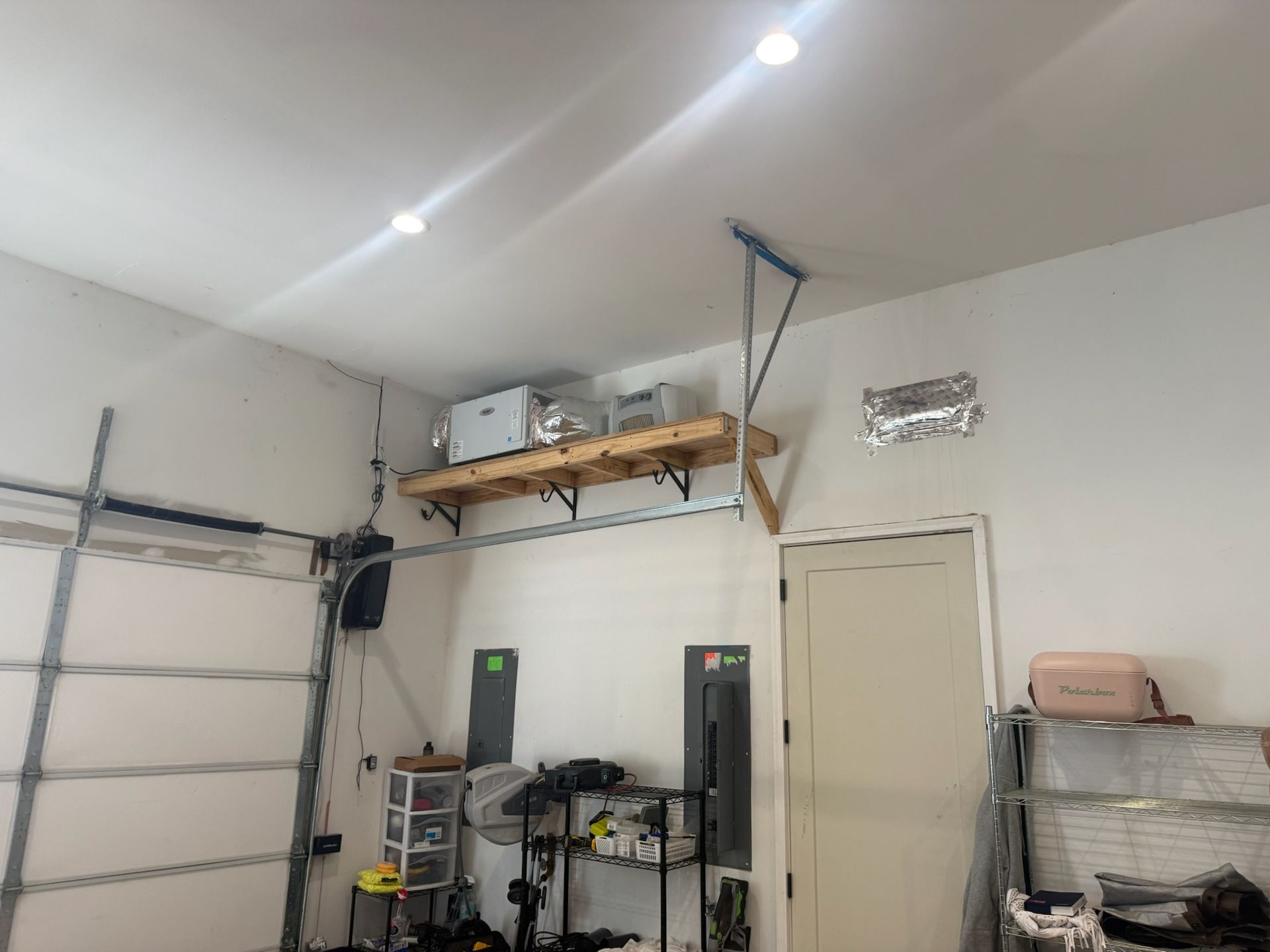 Garage interior with a wooden shelf holding items, a closed garage door on the left, and a door on the right.