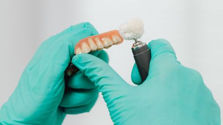 a person wearing green gloves is polishing a denture