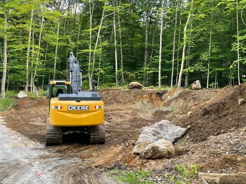A yellow excavator is driving down a dirt road in the woods.