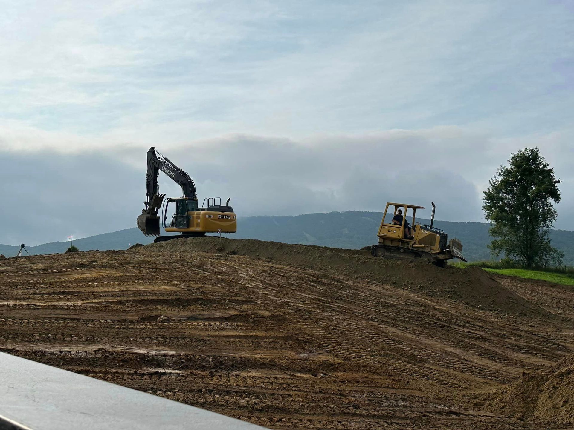 Two construction vehicles are working on a dirt field.