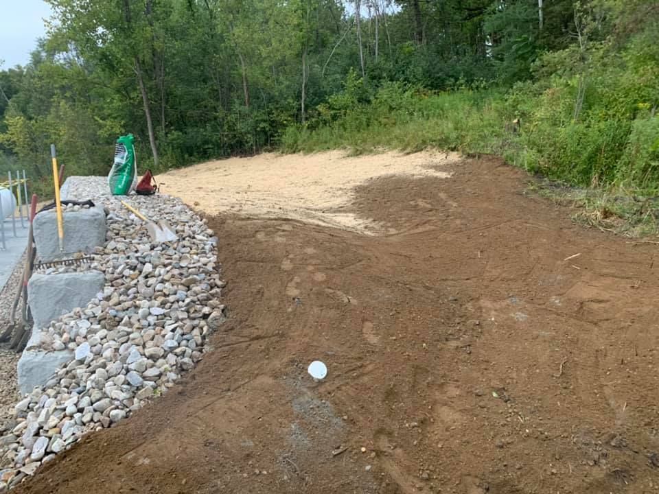 A dirt road with a stone wall and trees in the background.