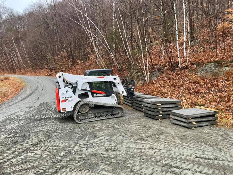 A bobcat is driving down a dirt road next to a pile of concrete slabs.