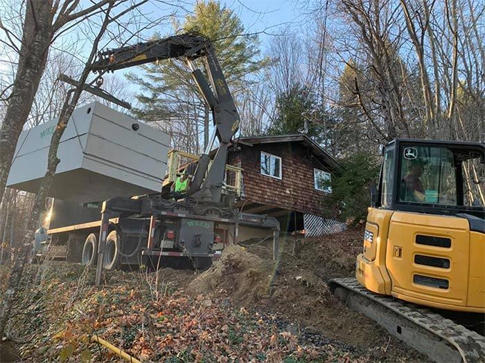 A bulldozer is loading a truck with a crane in front of a house.