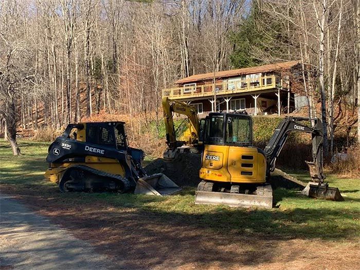 Two bulldozers are parked in front of a house in the woods.