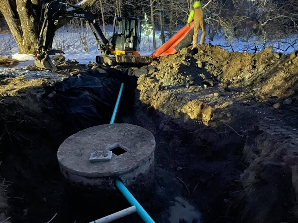 A man is standing on top of a pile of dirt next to a septic tank.