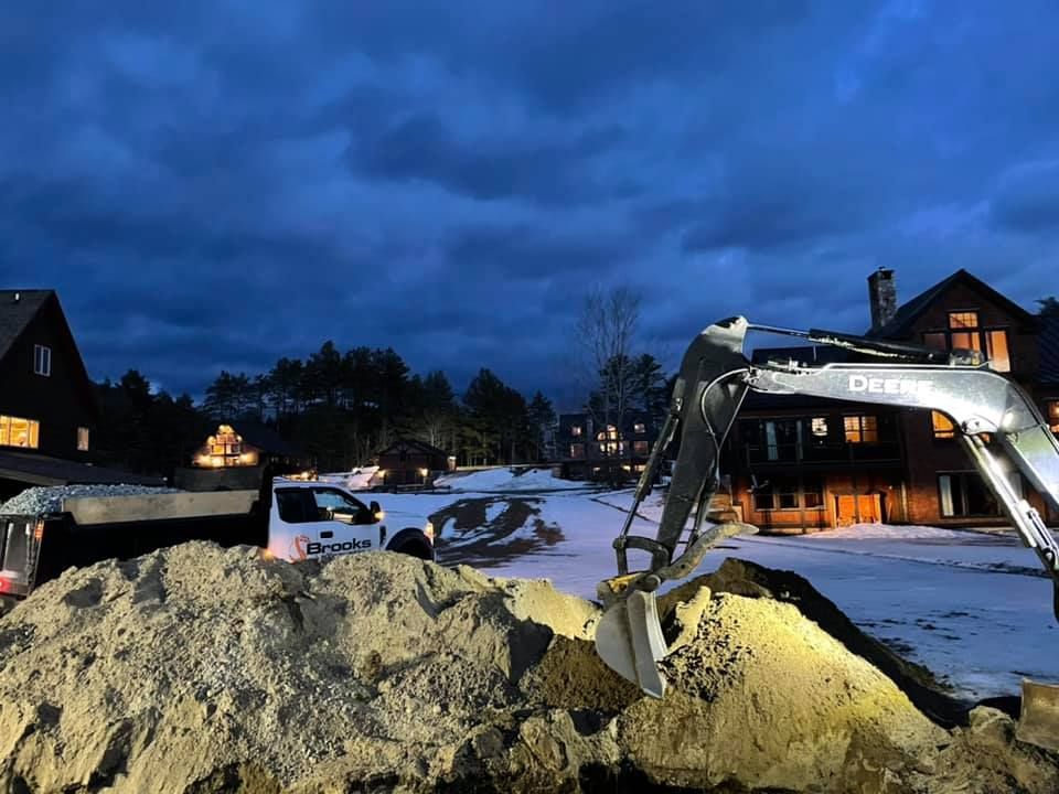 A large pile of dirt is being moved by an excavator at night.