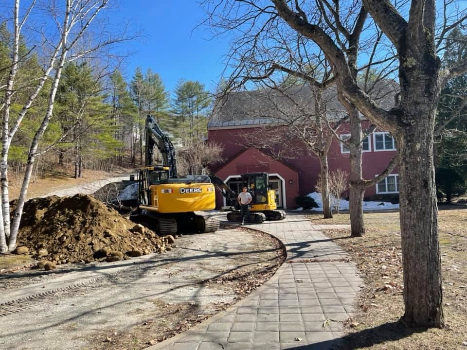 A yellow excavator is digging a hole in front of a red house.