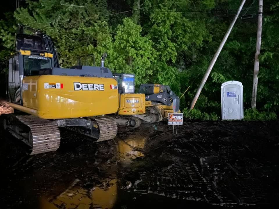A deere excavator is parked in a muddy area next to a portable toilet.