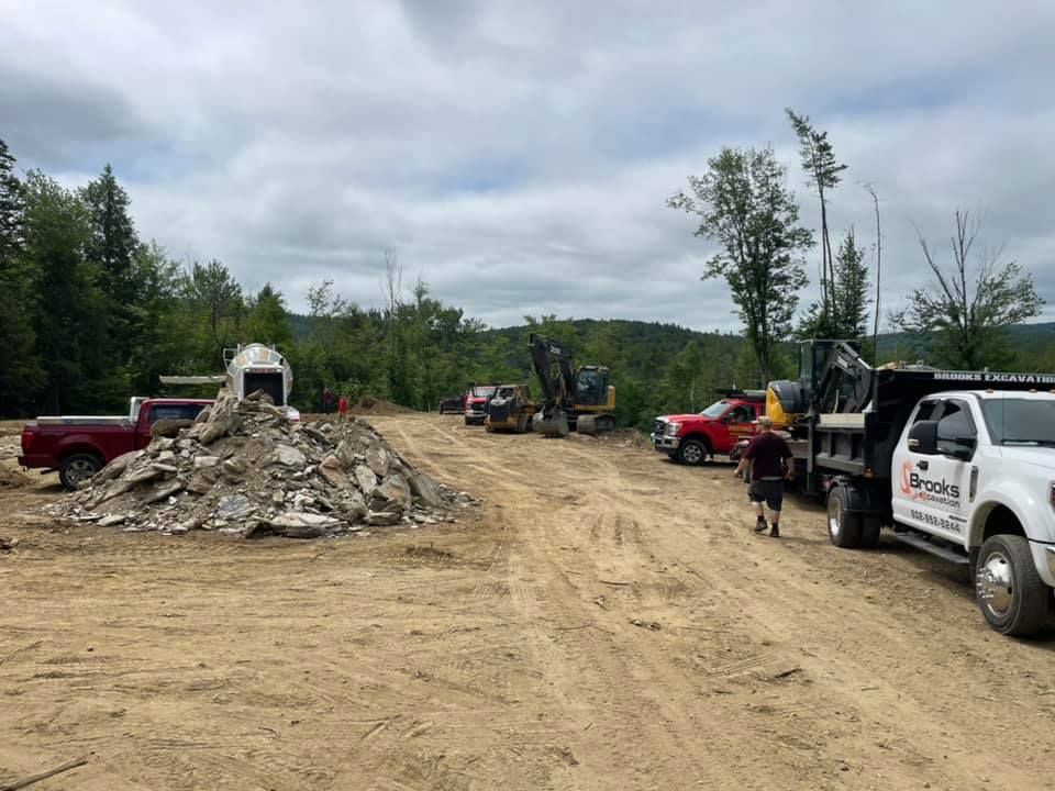A group of construction trucks are parked on the side of a dirt road.