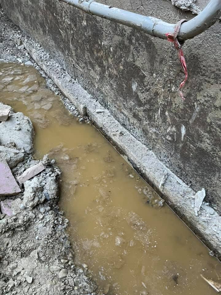 A muddy area next to a wall with a pipe coming out of it.
