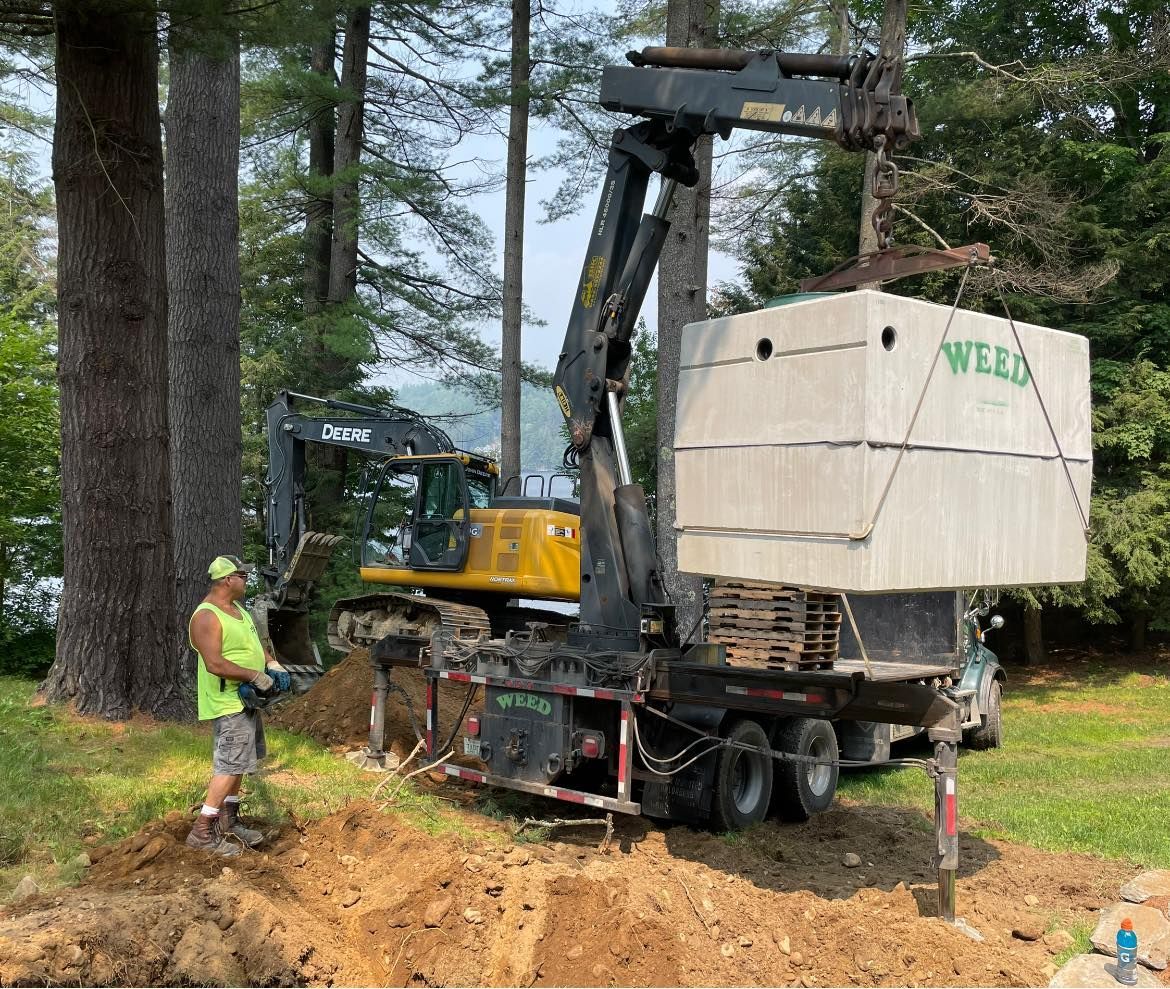 A man is standing in the dirt next to a truck carrying a septic tank.