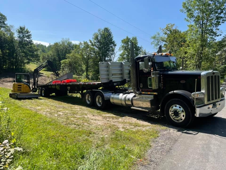 A semi truck is parked on the side of the road next to a small excavator.