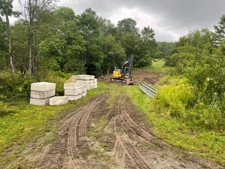 A bulldozer is driving down a dirt road in the middle of a forest.