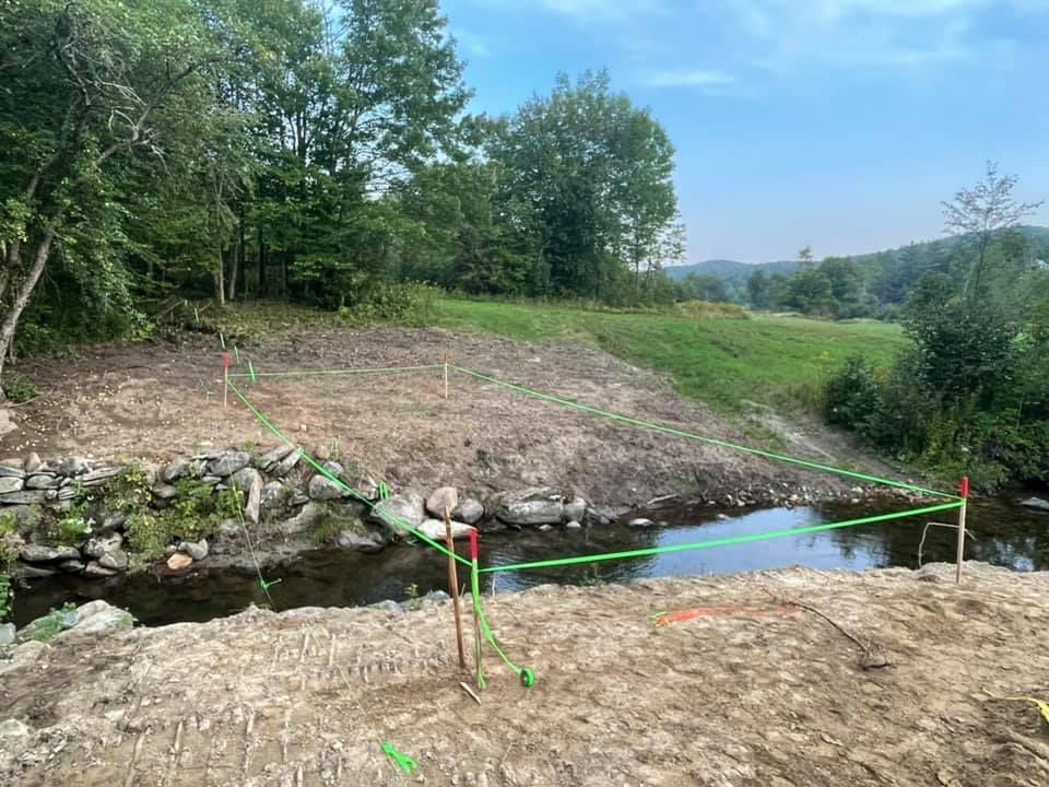 A river with a green fence around it and trees in the background.
