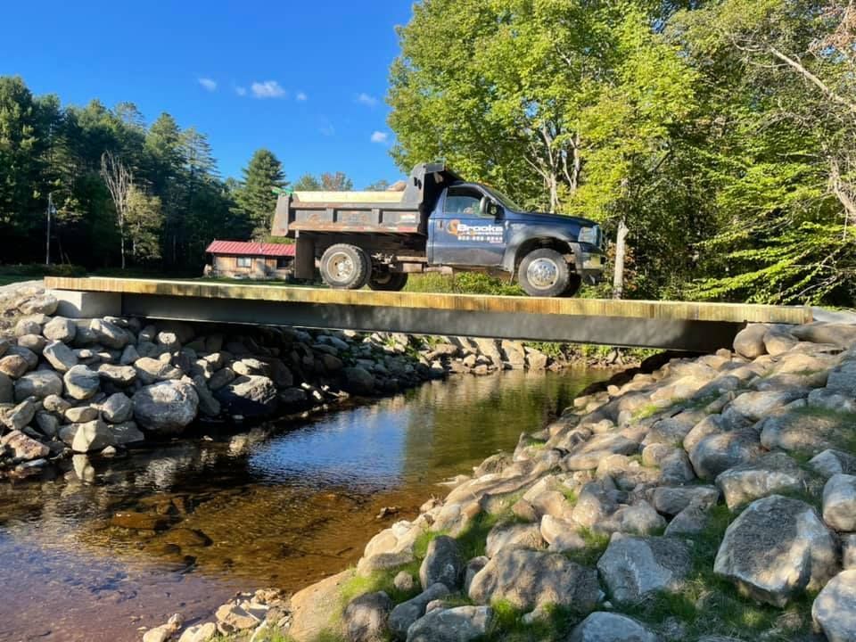 A dump truck is driving over a bridge over a river.
