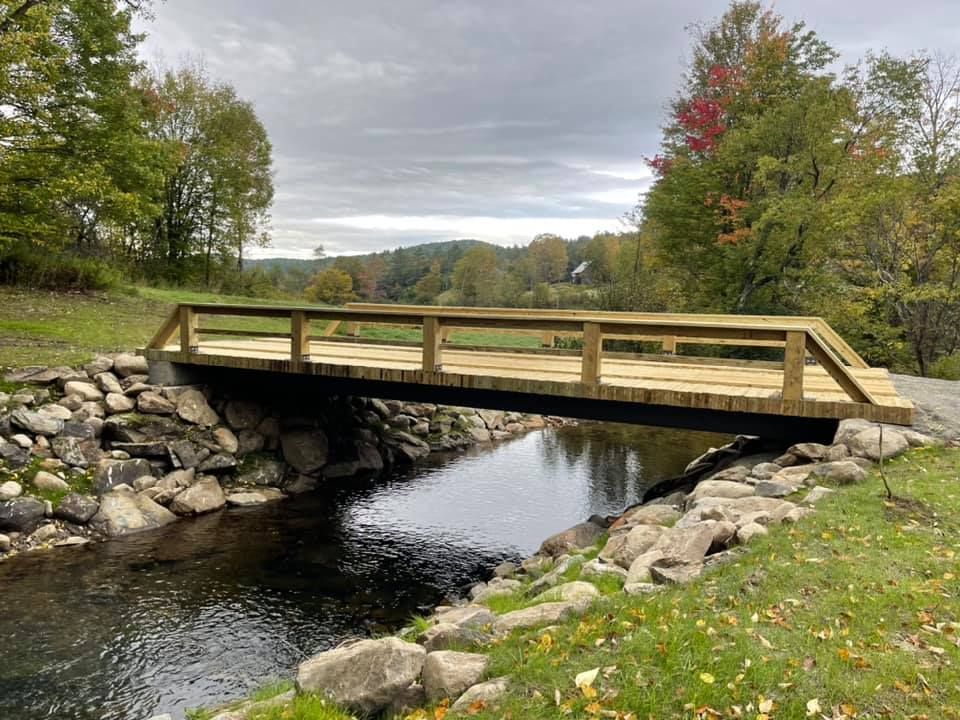 A wooden bridge over a river with trees in the background.