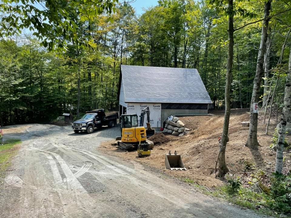 A house is being built in the middle of a forest next to a dirt road.