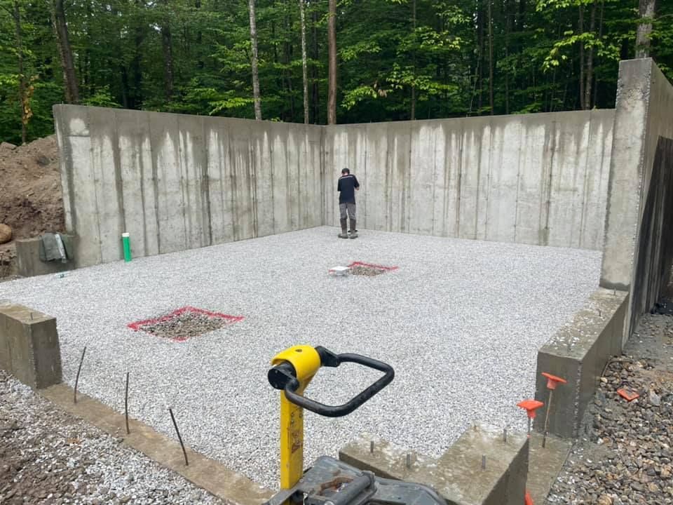 A man is standing in the middle of a gravel area in front of a concrete wall.