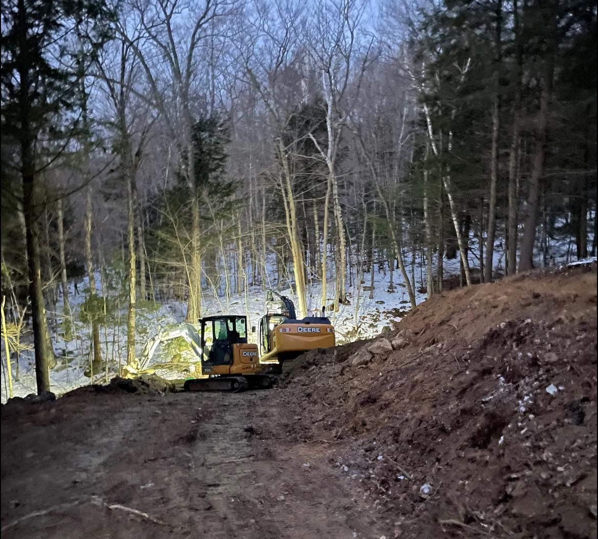 A yellow excavator is driving down a dirt road in the woods