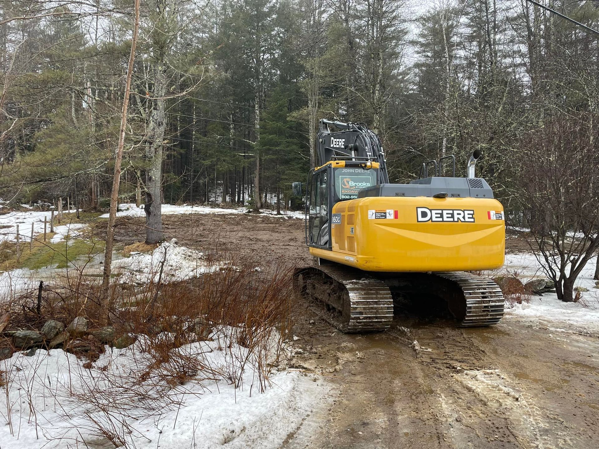 A yellow deere excavator is driving down a dirt road in the snow.