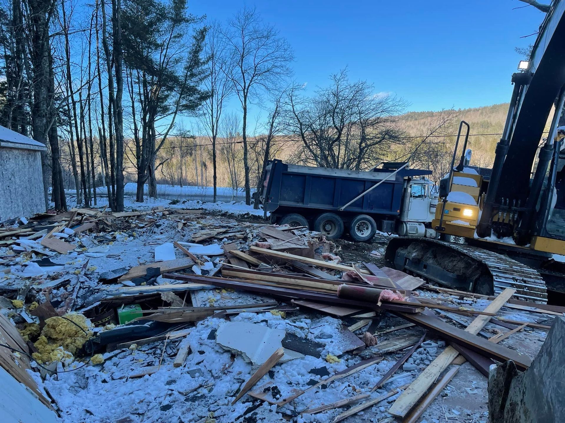 A dump truck is driving down a snowy road next to a pile of wood.