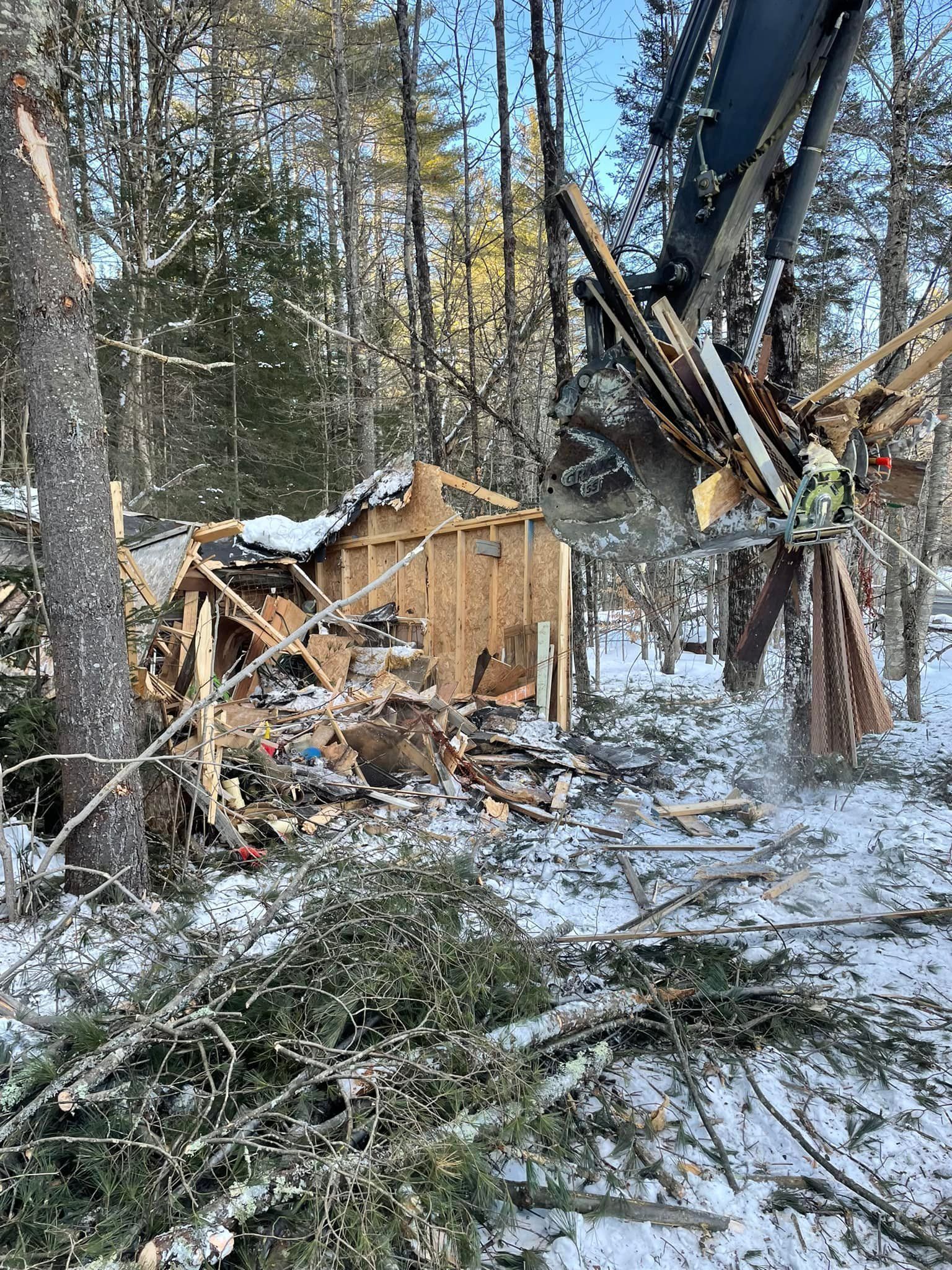 A crane is demolishing a house in the woods.
