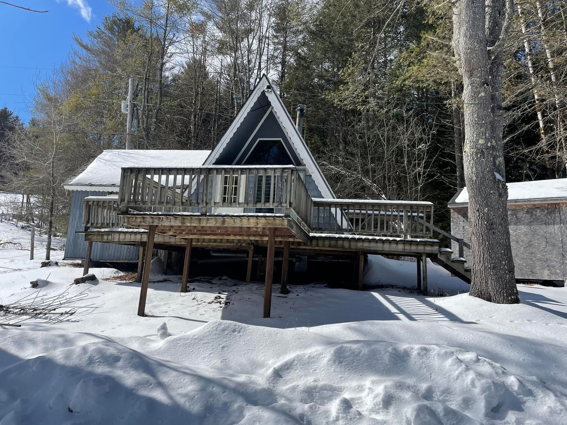 A house with a deck is surrounded by snow and trees.
