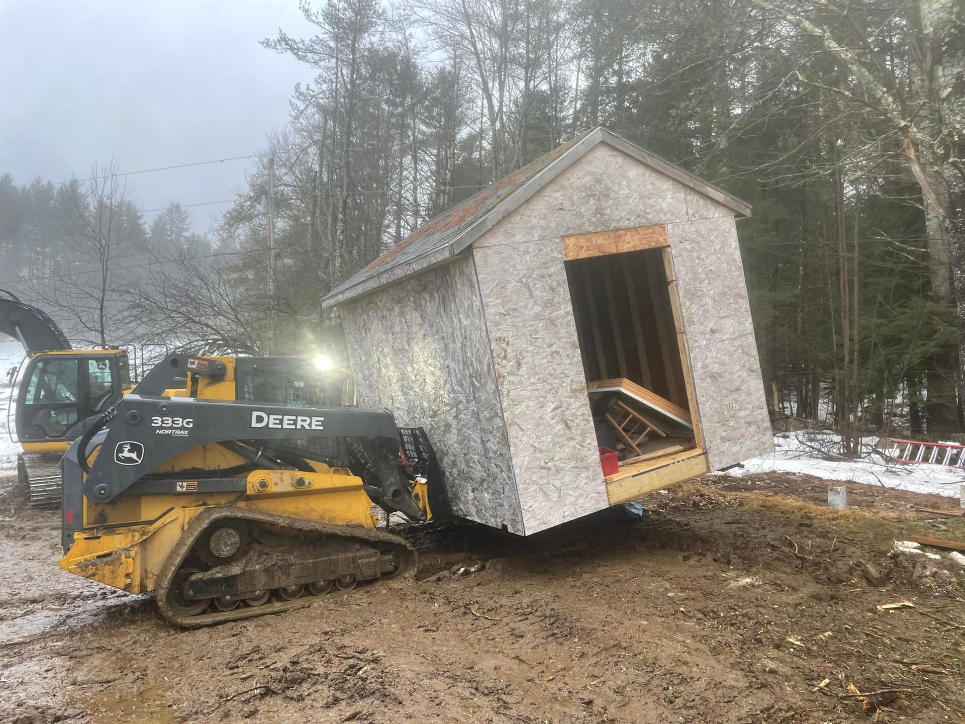 A small shed is being lifted by a bulldozer.