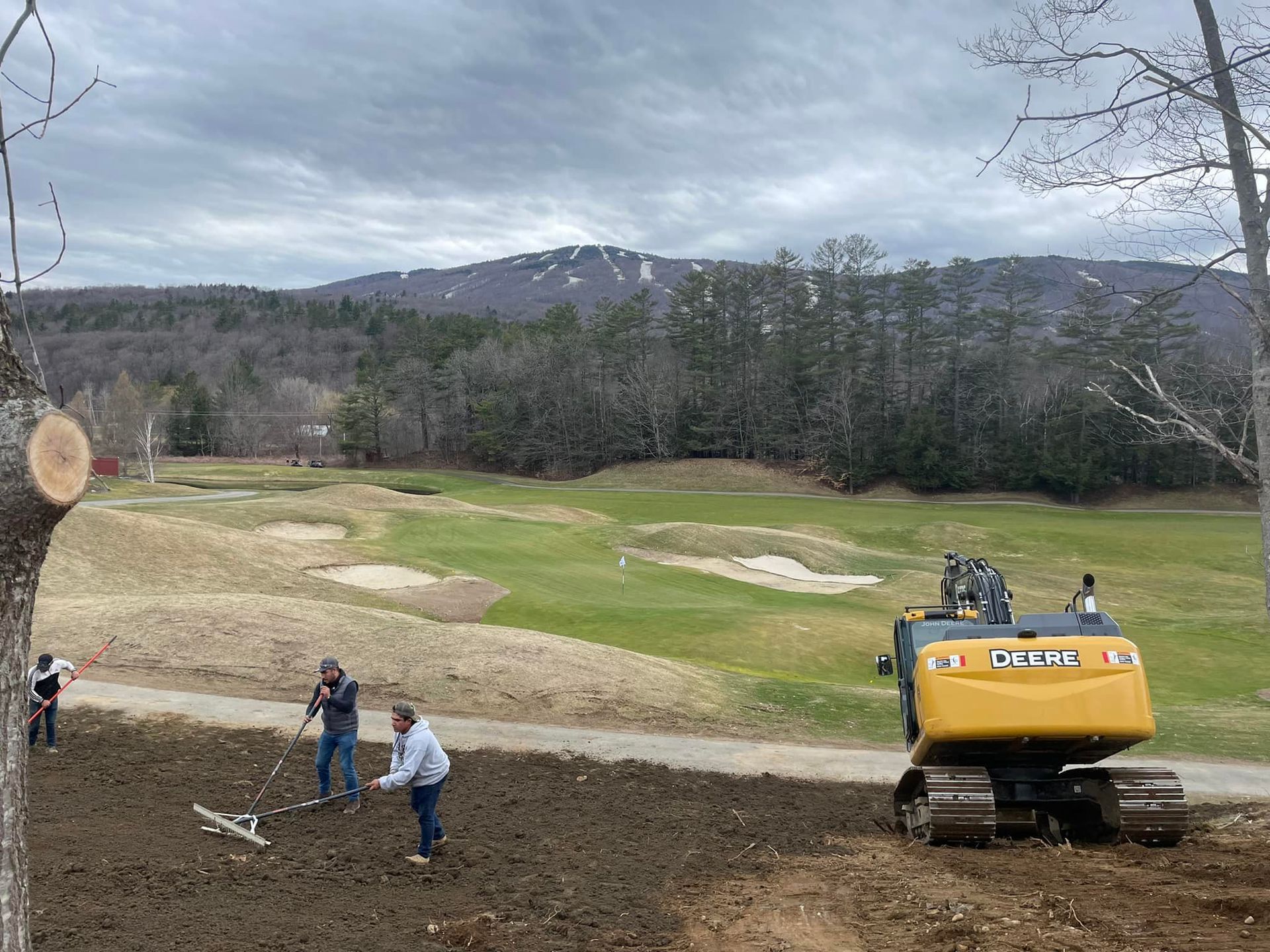 A group of people are working on a golf course with a bulldozer in the background.