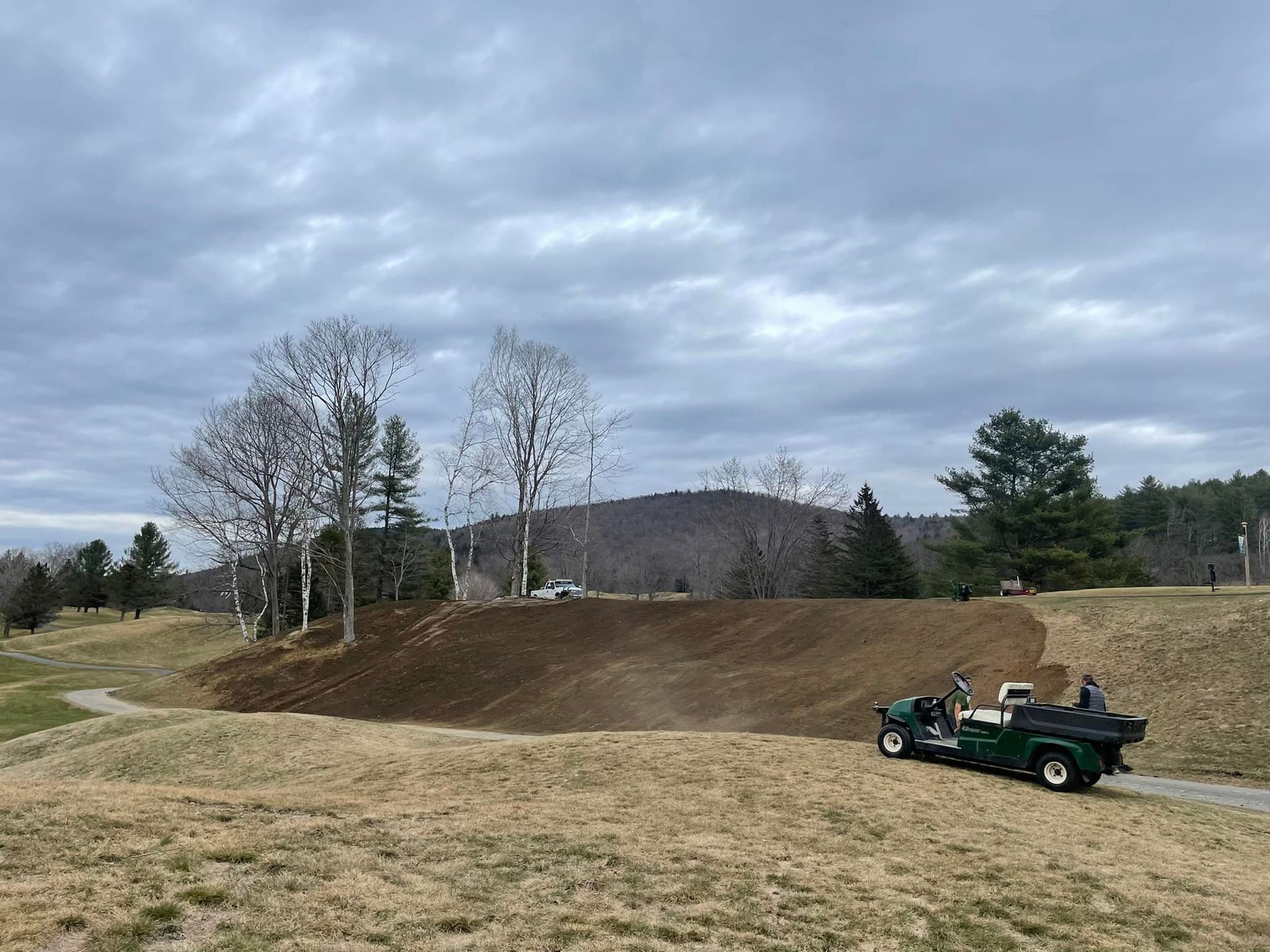 A green golf cart is driving down a dirt road.