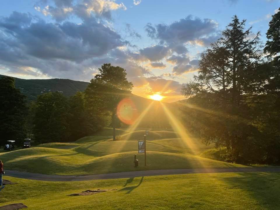 A sunset over a golf course with the sun shining through the trees