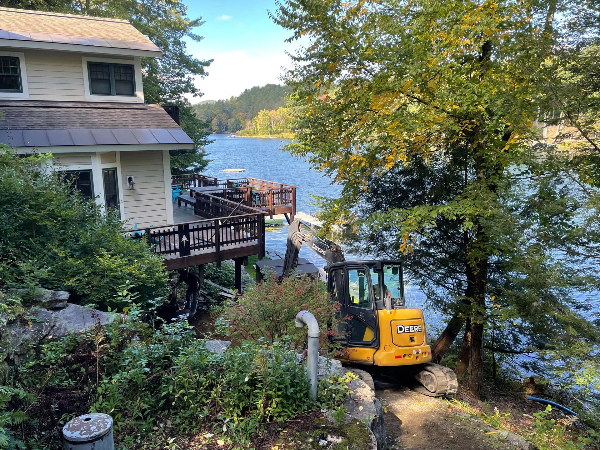 A yellow excavator is parked in front of a house next to a lake.