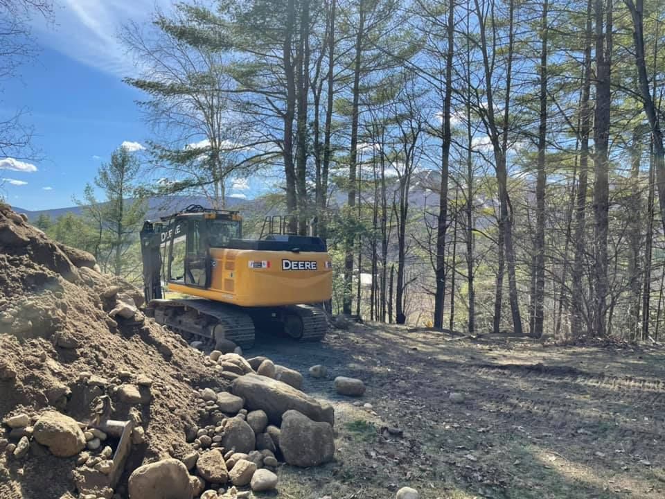 A yellow excavator is driving down a dirt road in the woods.