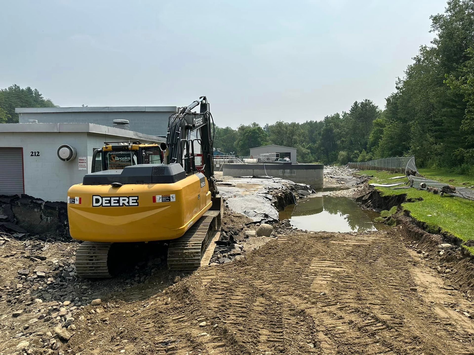 A yellow deere excavator is parked on a dirt road in front of a building.