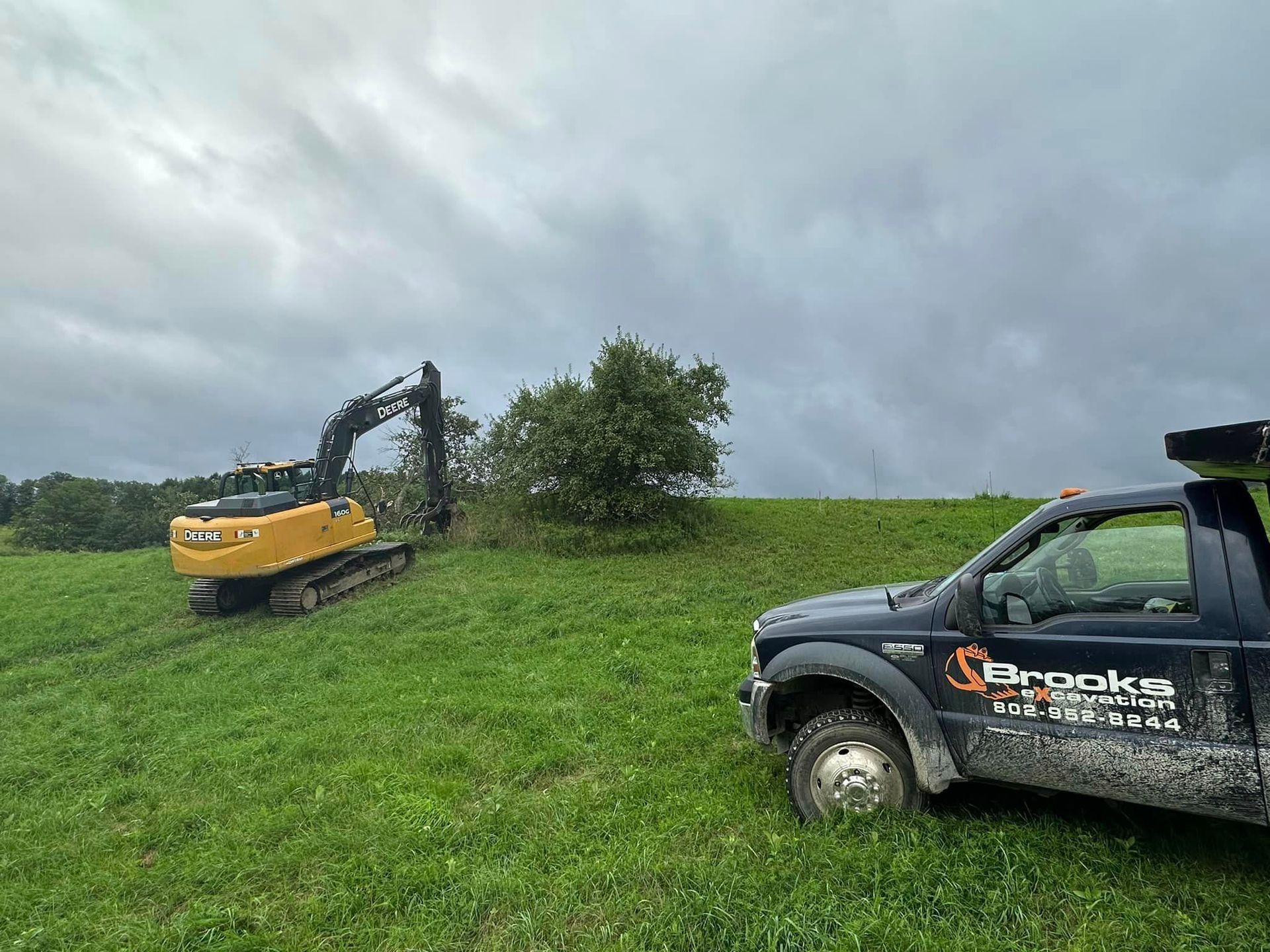 A truck is parked in a grassy field next to an excavator.