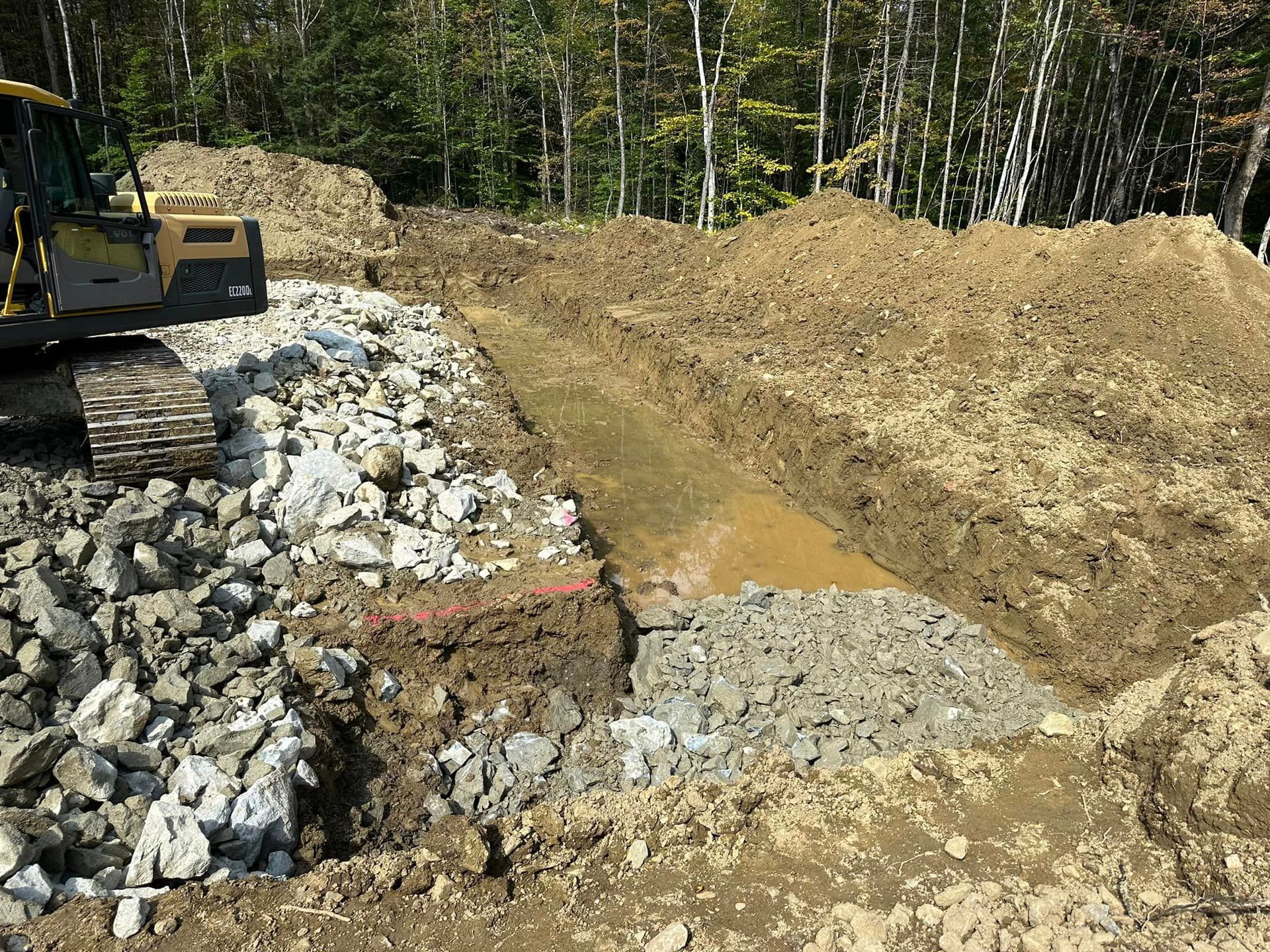 A bulldozer is digging a hole in the dirt near a pile of rocks.