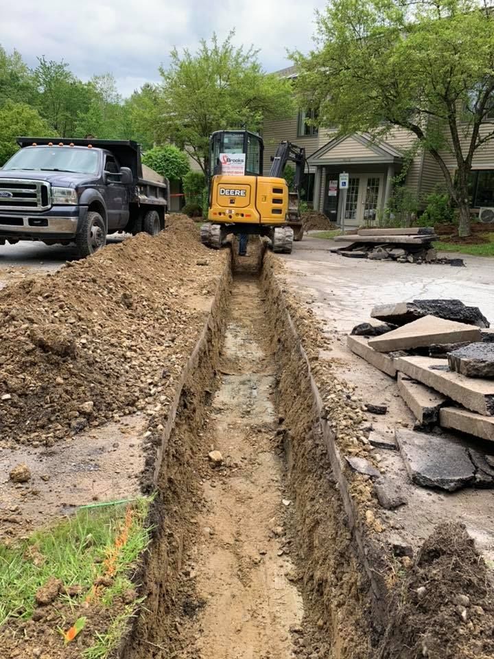 A truck is digging a trench in the dirt in front of a house.