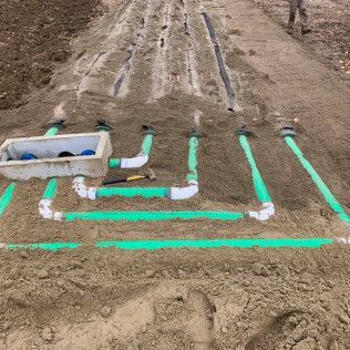 A bunch of green pipes are laying in the dirt.