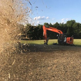 A large orange excavator is cutting grass in a field.