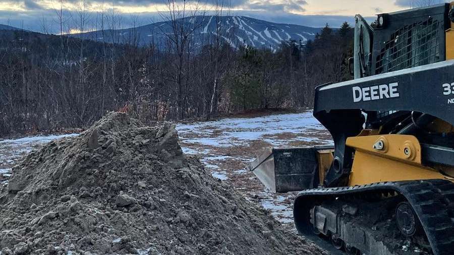 A deere bulldozer is moving dirt in a snowy field.