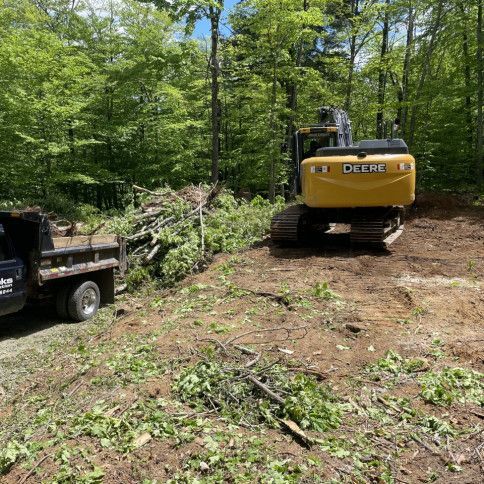 A yellow excavator is sitting on top of a dirt field next to a truck.