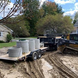 A trailer with concrete manholes on it is being towed by a bulldozer.