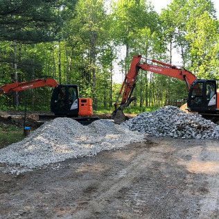 Two excavators are working on a pile of rocks in a dirt field.