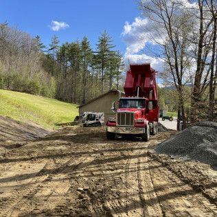 A red dump truck is driving down a dirt road.